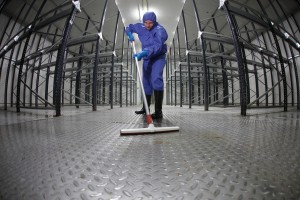 worker in protective uniform cleaning floor in empty storehouse